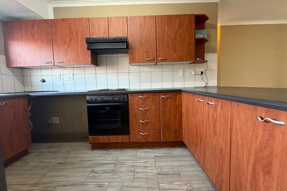 A dated kitchen featuring wood-look laminate cabinetry, dark countertops, and tiled flooring, requiring minor repairs and cosmetic updates to modernize the space.
