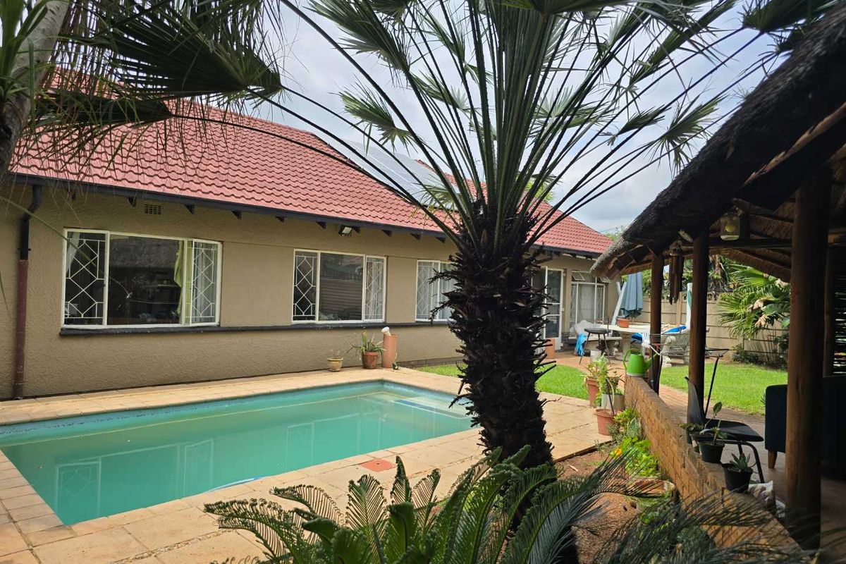Rear view of the property featuring a swimming pool, paved surround, and a covered outdoor entertainment area with a thatched roof.