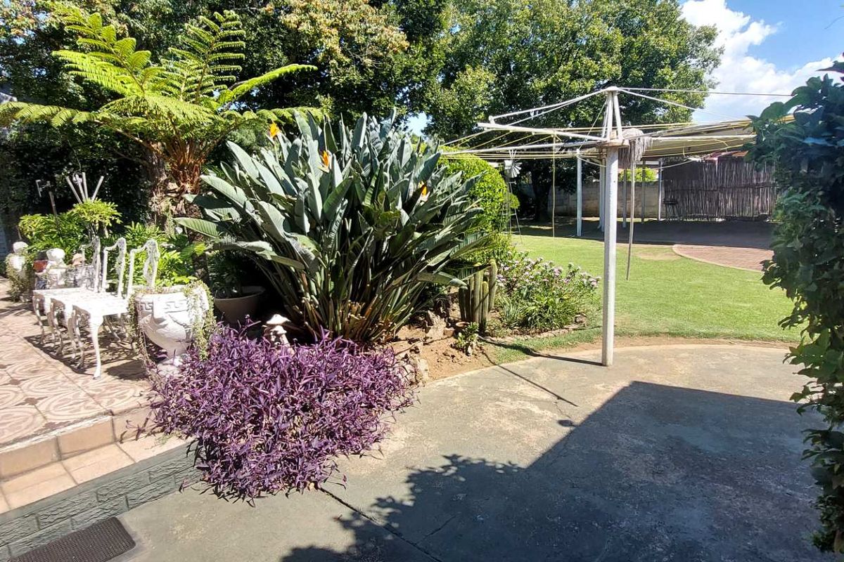 A spacious rear garden featuring a paved patio area, established landscaping, and a lawn, providing a functional outdoor space for relaxation and recreation.