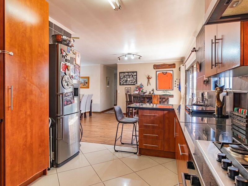 Open-plan kitchen and living area featuring warm-toned cabinetry, granite countertops, gas hob, and a seamless transition between tiled kitchen and laminate living room flooring.