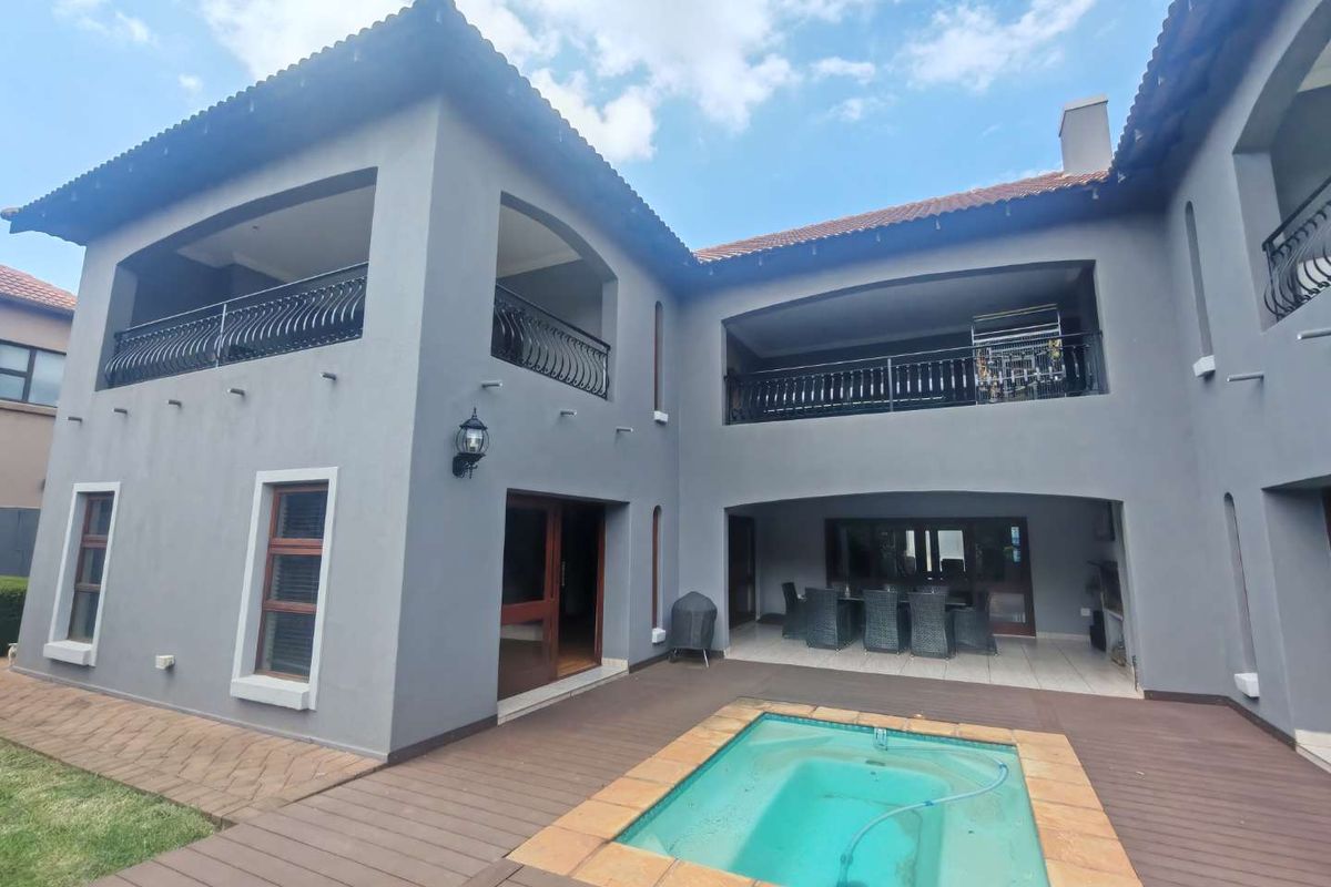 Rear view of a two-story house featuring a covered patio, upper-level balconies with wrought iron railings, and a built-in swimming pool with decking.