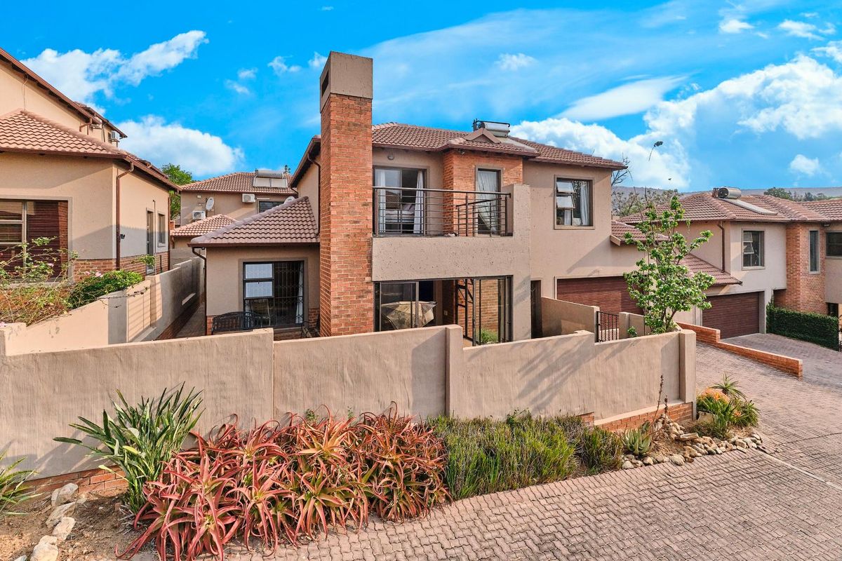 A view of the rear exterior of a townhouse featuring a brick chimney, balcony, and paved courtyard area.