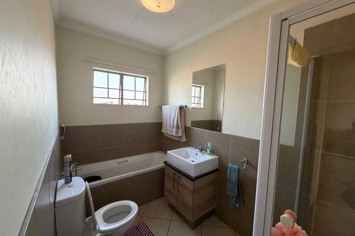 A functional bathroom featuring a bathtub, separate shower enclosure, vanity basin, and toilet with neutral wall and floor tiling.