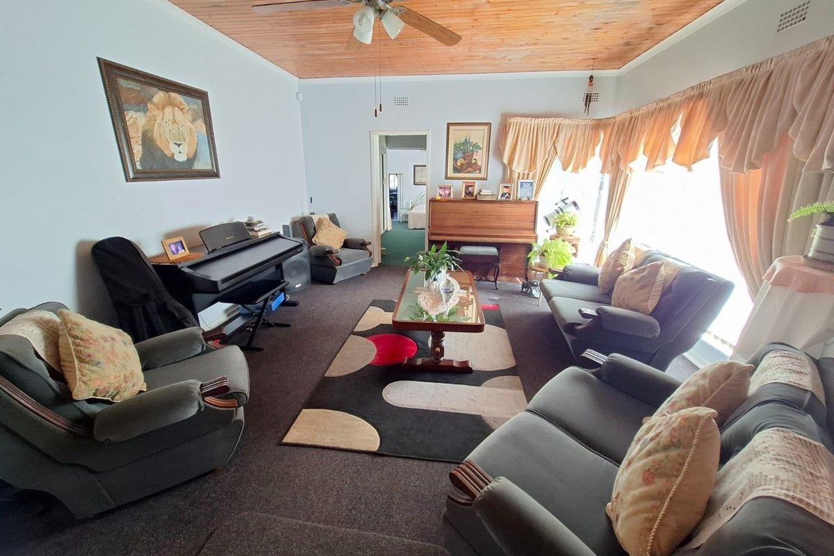A spacious living room featuring a warm timber-paneled ceiling, a central ceiling fan, and large windows that provide ample natural light.