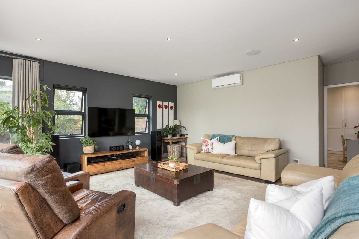 A well-maintained living room featuring recessed downlights, ceiling speakers, and a wall-mounted split-system air conditioner, with large windows providing natural light.