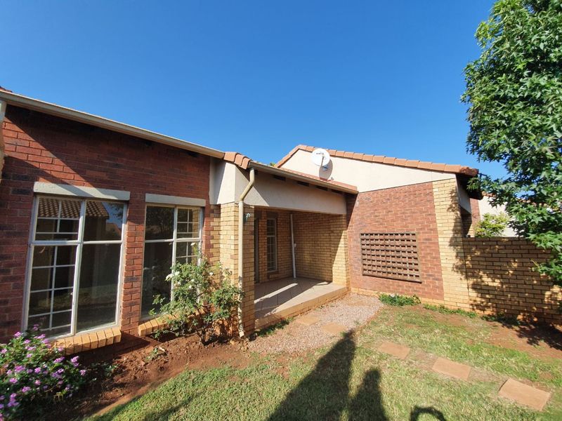 A rear view of a face brick townhouse featuring a covered patio, tiled roof, and a small private garden area.