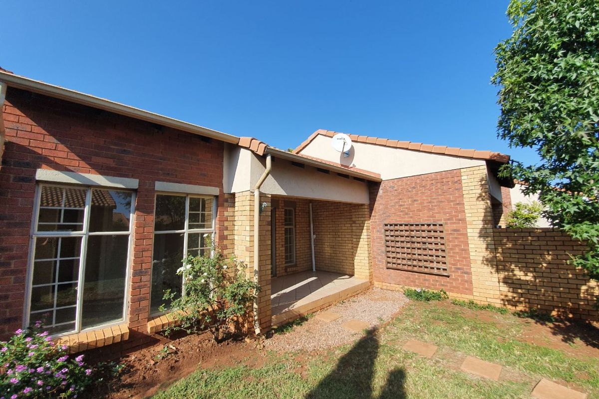 A rear view of a face brick townhouse featuring a covered patio, tiled roof, and a small private garden area.