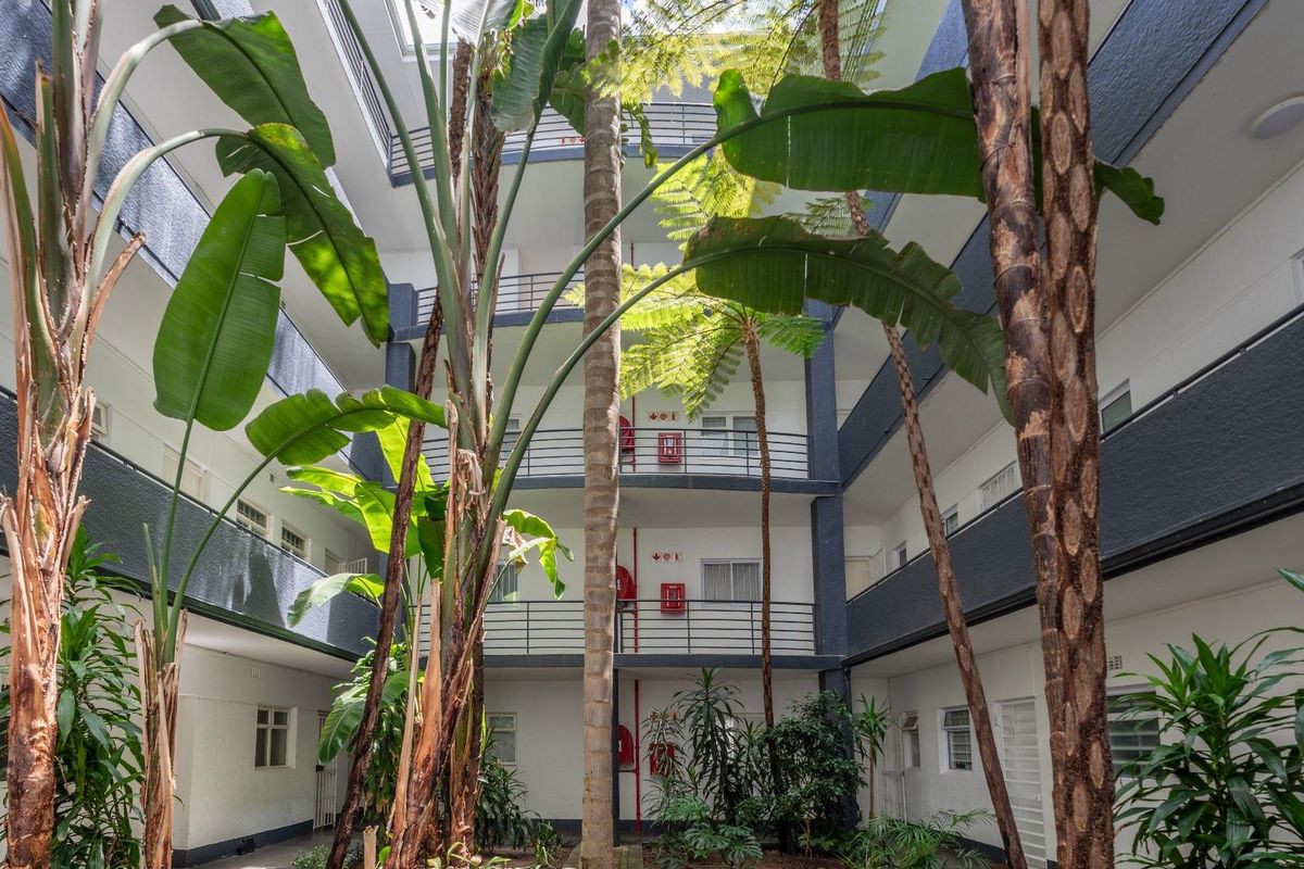 A central open-air atrium courtyard within an apartment complex, featuring multi-level walkways, metal railings, and established tropical landscaping.