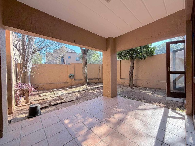 A covered patio area featuring tiled flooring, leading out to a private garden space enclosed by boundary walls.