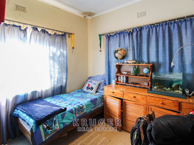 A bedroom featuring natural light through windows with curtain rails and visible ceiling water damage requiring attention.