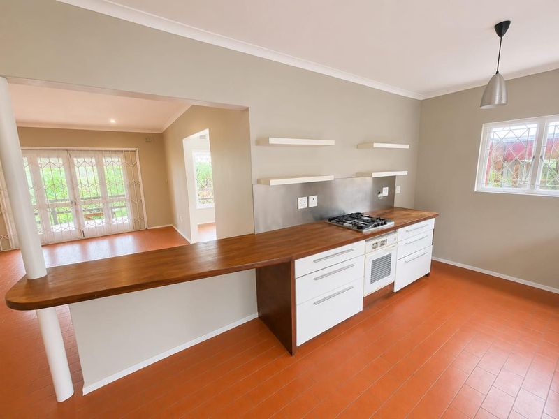 A bright, open-plan kitchen featuring wooden countertops, a built-in oven with gas hob, stainless steel splashback, and floating shelves.