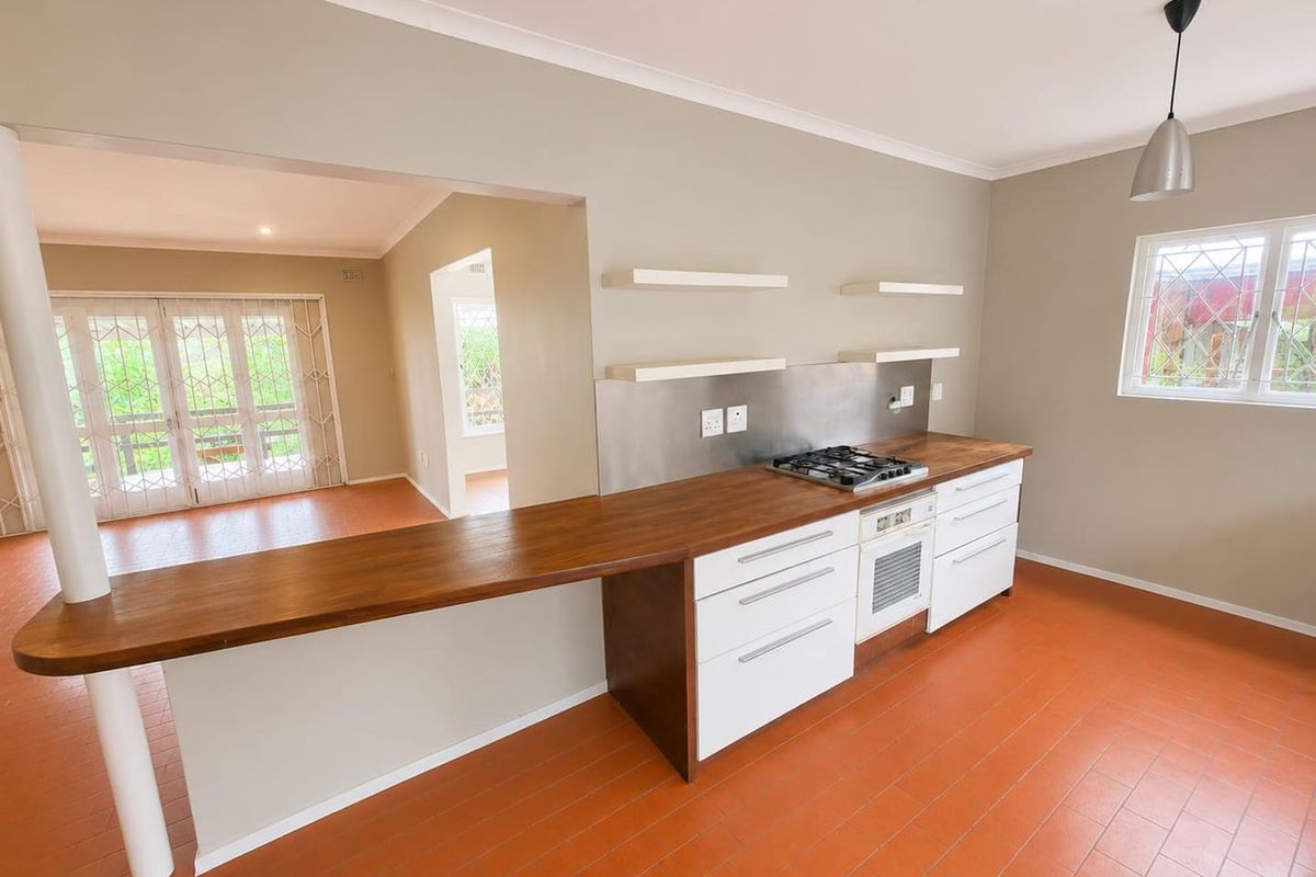 A bright, open-plan kitchen featuring wooden countertops, a built-in oven with gas hob, stainless steel splashback, and floating shelves.