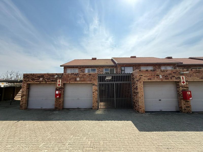 Front elevation of a cluster complex featuring face brick construction, multiple roller shutter garage doors, and a paved driveway area.