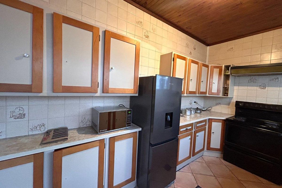 A dated kitchen featuring timber-framed cabinetry, tiled splashbacks, a timber-paneled ceiling, and tiled flooring.