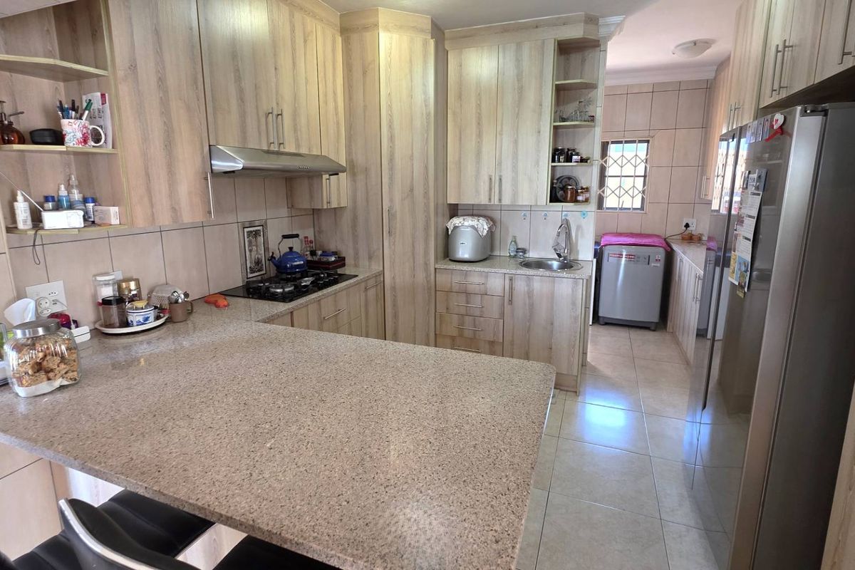 A functional kitchen featuring light wood-grain cabinetry, granite countertops, a built-in gas hob with extractor fan, and an adjoining scullery area.
