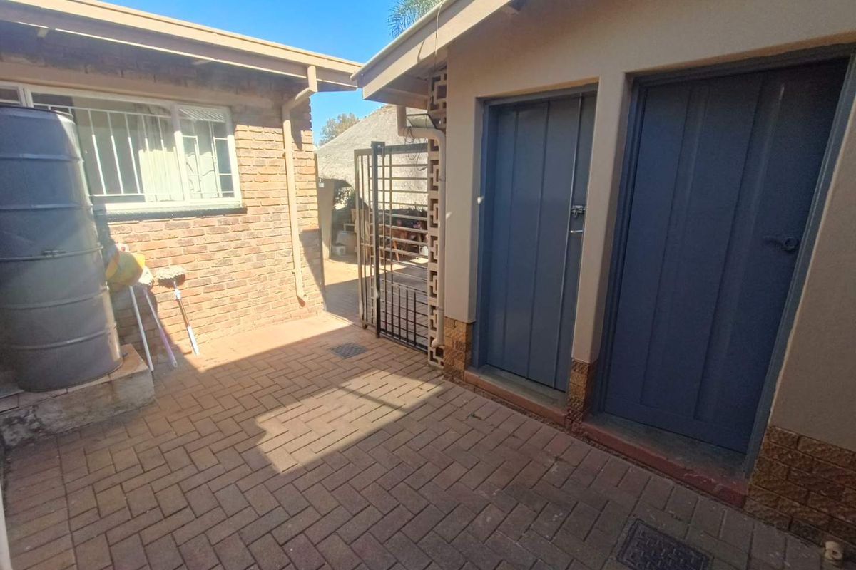 A paved outdoor courtyard area featuring brick walls, secure metal gates, and access to utility or storage doors.