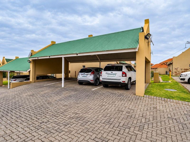 A covered carport area with a green corrugated metal roof and paved driveway, providing sheltered parking for multiple vehicles.