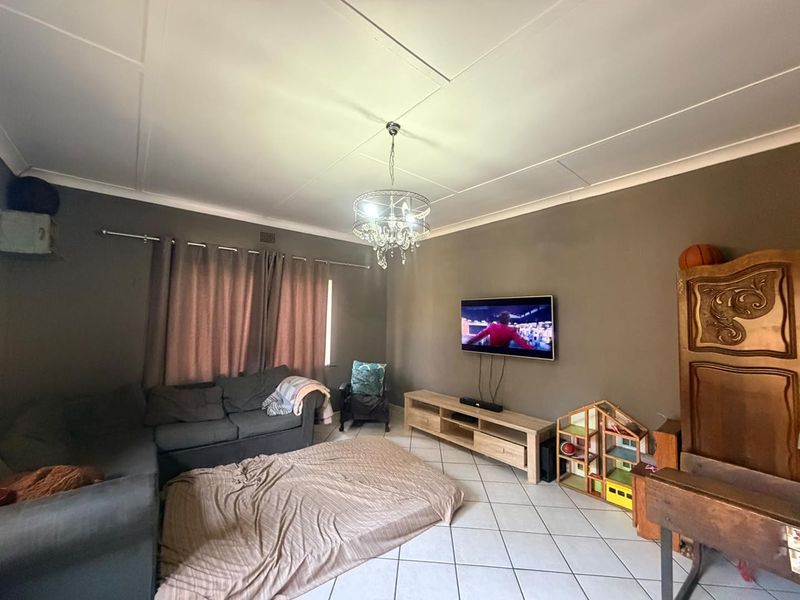 A living room featuring tiled flooring, coving, and a central ceiling light fixture, with a wall-mounted television as the focal point.