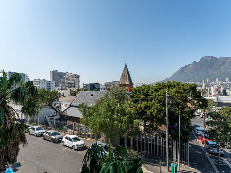 An elevated urban view overlooking the surrounding neighbourhood, featuring city buildings, a historic church spire, and mountain scenery in the distance.