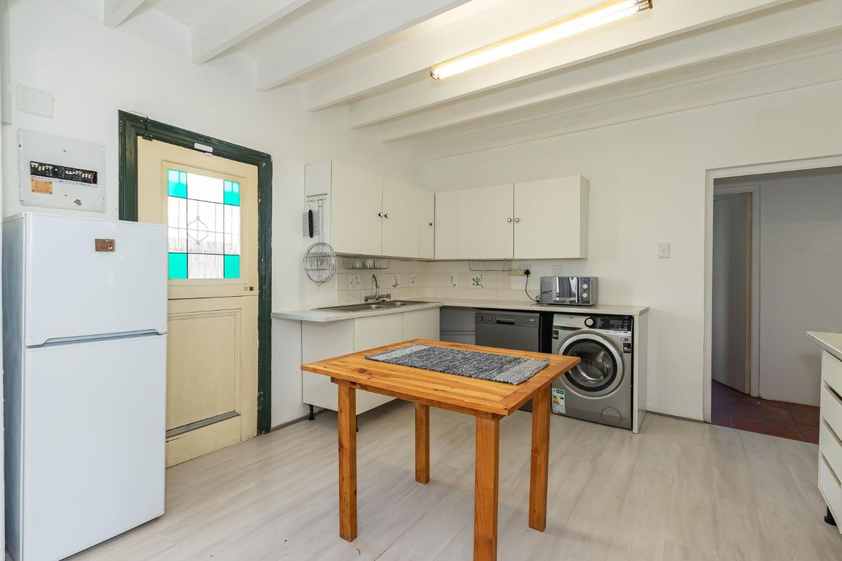A functional kitchen and laundry area featuring white cabinetry, a stainless steel sink, and space for integrated appliances under the counter.