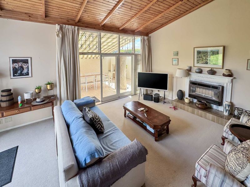Spacious living room featuring an exposed timber raked ceiling, a built-in fireplace with a tiled hearth, and large glass sliding doors leading to the patio.
