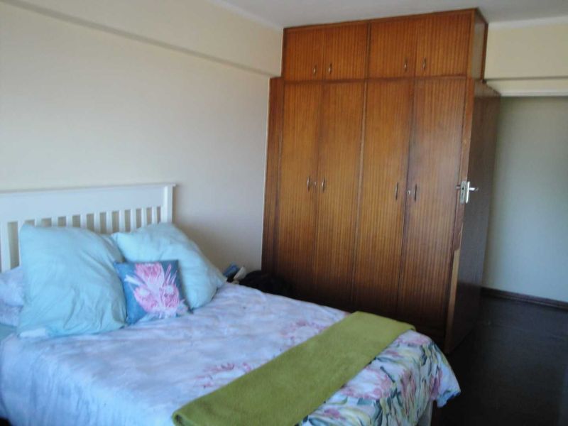 A bedroom featuring a large, floor-to-ceiling built-in wooden wardrobe with overhead storage compartments.
