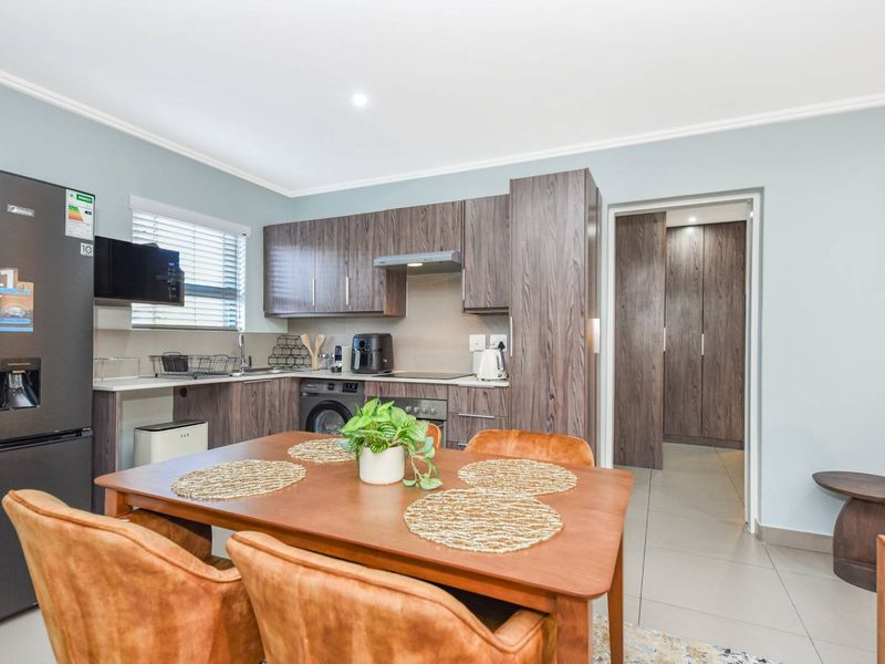 Modern open-plan kitchen and dining area featuring contemporary wood-grain cabinetry, integrated appliances, and sleek tiled flooring, leading into a hallway with built-in storage.