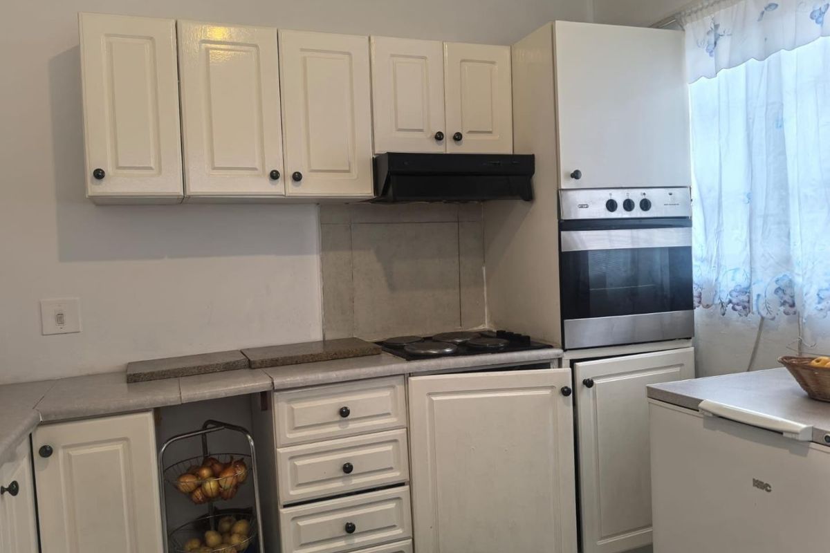 A dated kitchen featuring white cabinetry, built-in oven, electric hob, and extractor fan, offering potential for a modern renovation.