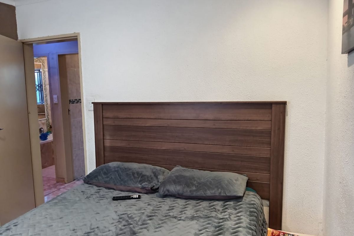 A bedroom featuring a wooden headboard with an adjacent doorway leading to a tiled bathroom.