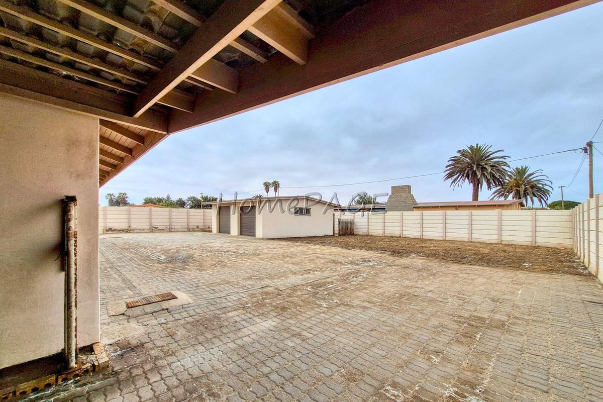 Spacious paved backyard area featuring a covered patio, perimeter boundary walls, and a detached garage structure.