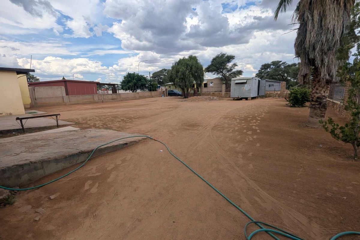 Expansive outdoor yard area featuring a large unpaved ground surface, perimeter boundary walls, and basic exterior building access.