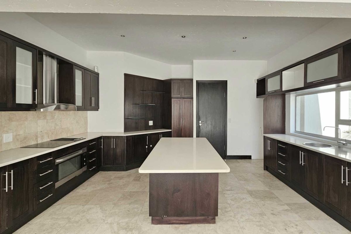 Spacious modern kitchen featuring dark wood cabinetry, stone countertops, a central island, built-in oven, and tiled flooring throughout.