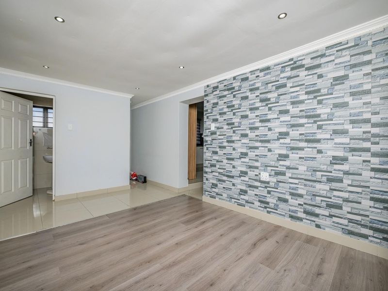 Spacious living area featuring a decorative stone-effect feature wall, a combination of laminate and tiled flooring, and modern recessed downlighting.