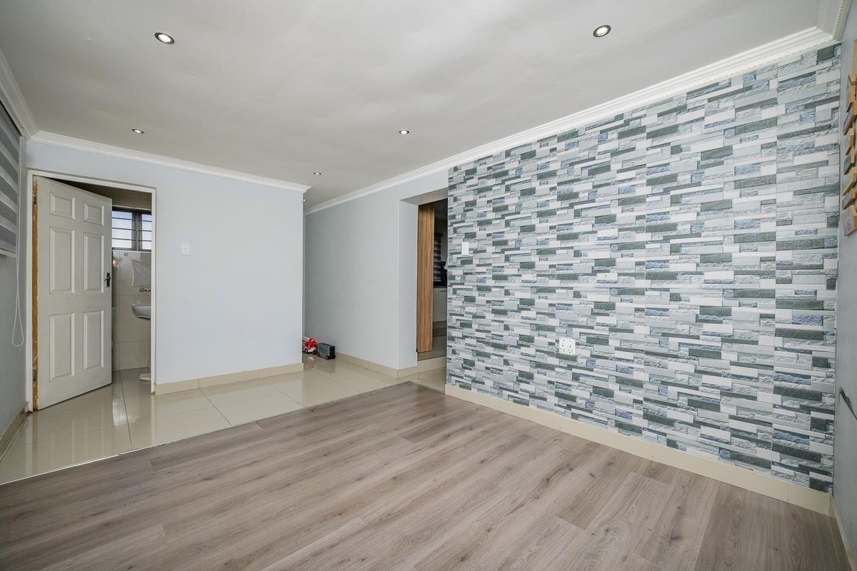 Spacious living area featuring a decorative stone-effect feature wall, a combination of laminate and tiled flooring, and modern recessed downlighting.