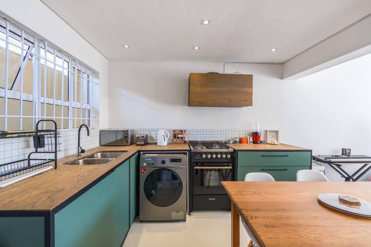 Modern kitchen featuring green cabinetry, wooden countertops, a double sink, gas hob with extractor, and integrated laundry appliance space.