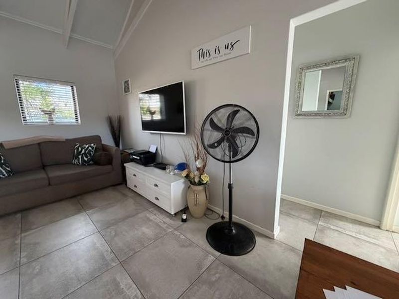 A bright living room featuring large format floor tiles, a vaulted ceiling, and a neutral color palette, providing a clean and functional living space.