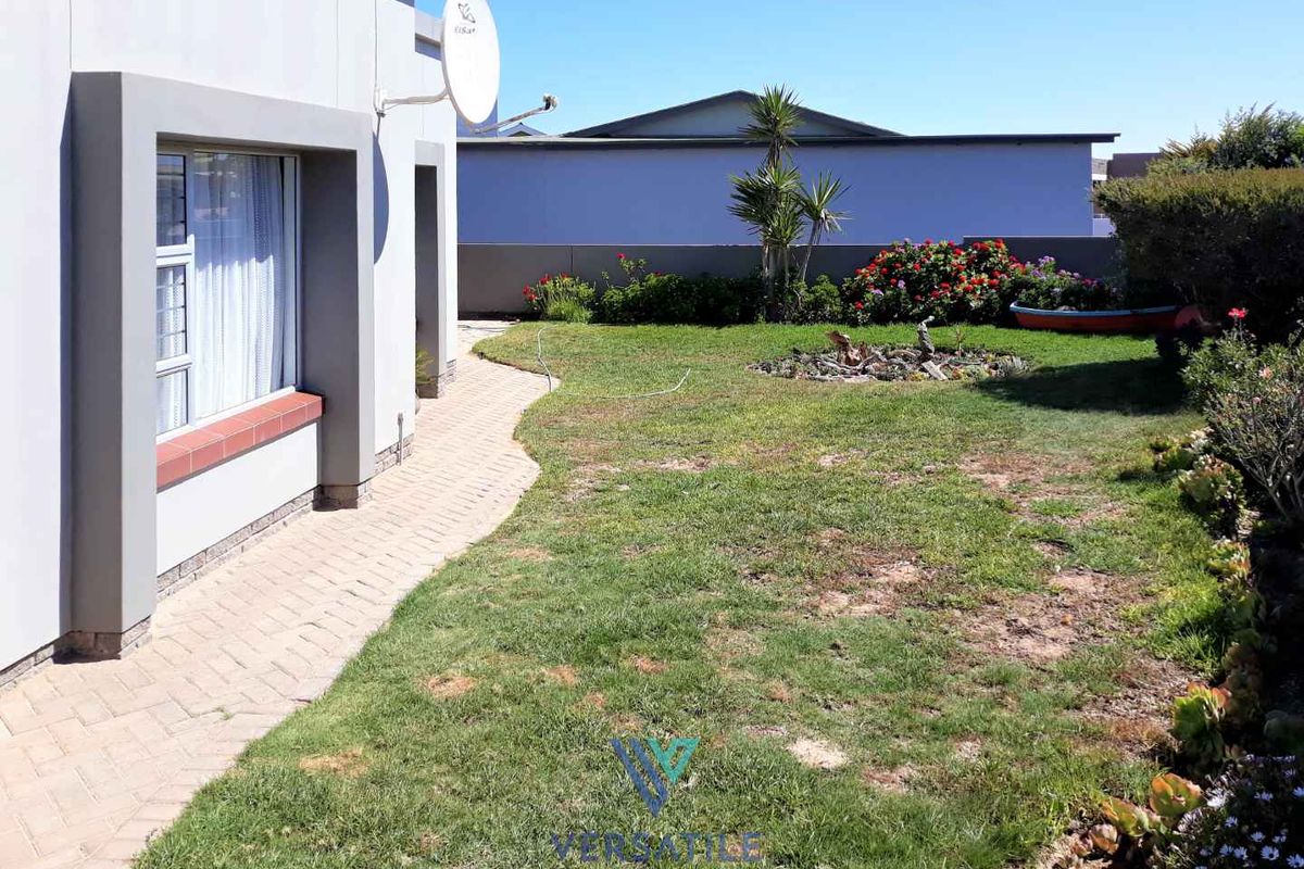 A rear garden area featuring a paved walkway, established lawn, and perimeter boundary wall.