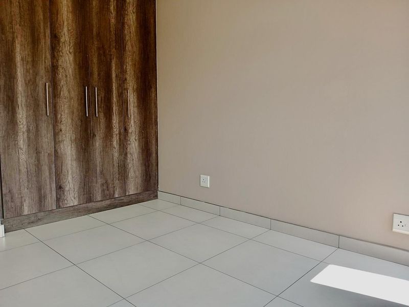 A clean, empty bedroom featuring modern wood-finish built-in cupboards and neutral tiled flooring.