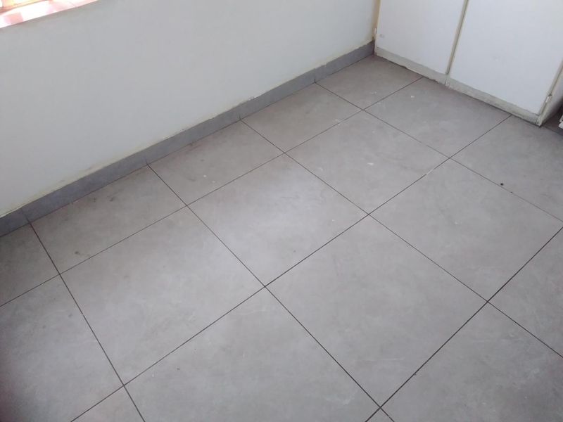 An empty bedroom featuring neutral tiled flooring and built-in cupboard storage, providing a clean and versatile space ready for personalization.