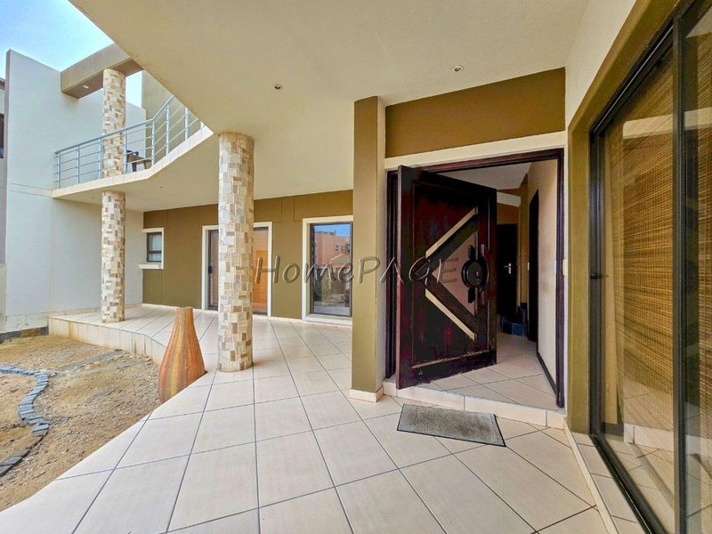 Covered patio area featuring stone-clad columns, tiled flooring, and a modern pivot entrance door, leading to an upper-level balcony.
