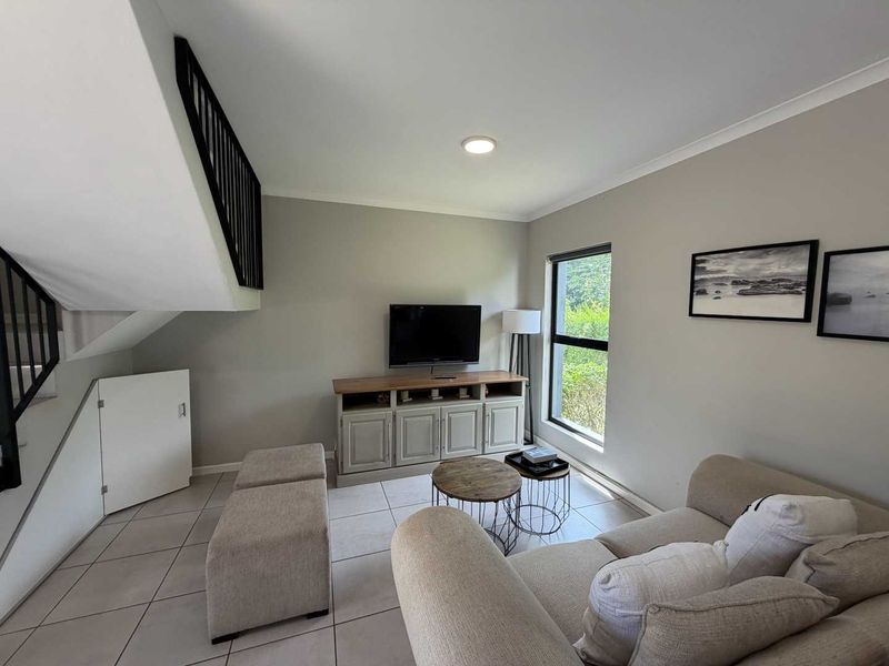 A bright living room featuring tiled flooring, a staircase with a black railing, and convenient under-stair storage, creating a functional and open living space.