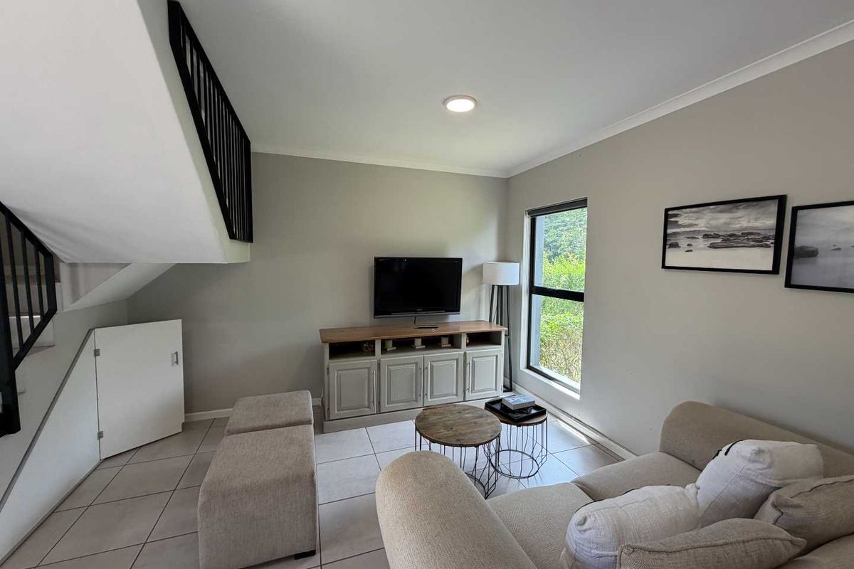 A bright living room featuring tiled flooring, a staircase with a black railing, and convenient under-stair storage, creating a functional and open living space.