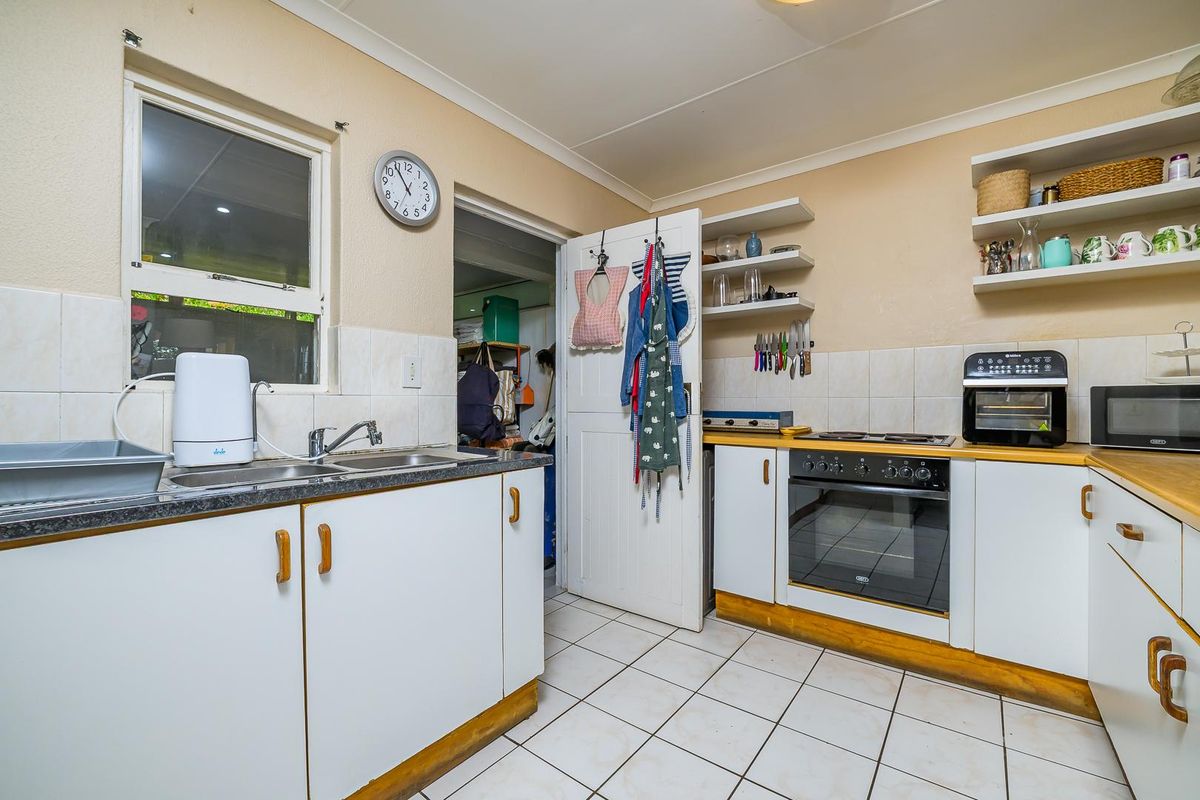 A functional kitchen featuring white cabinetry, tiled splashbacks, a built-in oven with hob, and a double stainless steel sink.