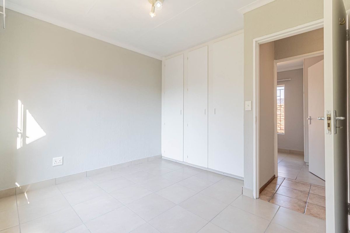 A bright, empty bedroom featuring neutral tiled flooring, built-in cupboards, and a doorway leading to an adjacent room.