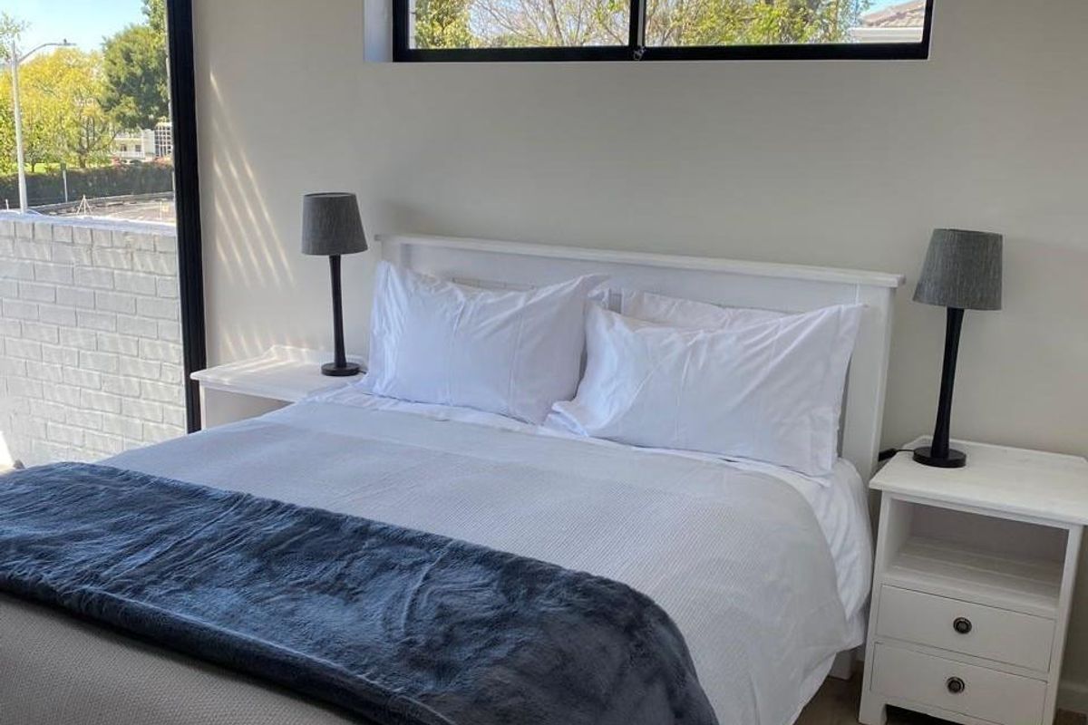A bright and modern bedroom featuring laminate flooring, a large sliding glass door, and a horizontal window providing natural light.