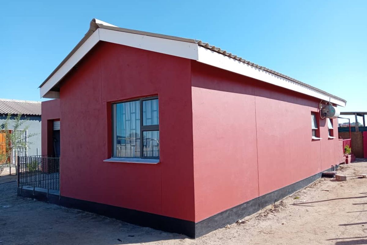 A side view of a detached house featuring red painted exterior walls, a pitched roof, and metal security bars on the windows.