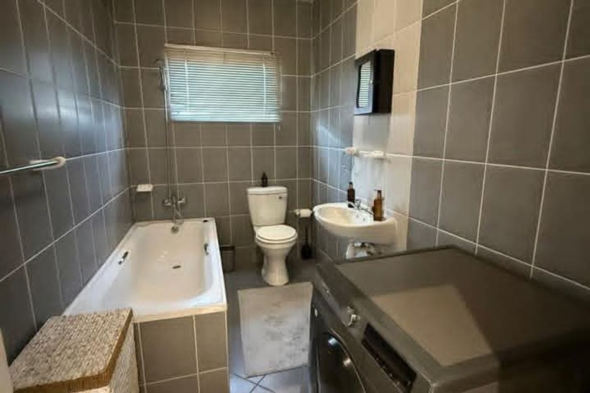 A functional bathroom featuring a built-in bathtub, wall-mounted basin, and toilet, finished with neutral grey and white wall tiling.