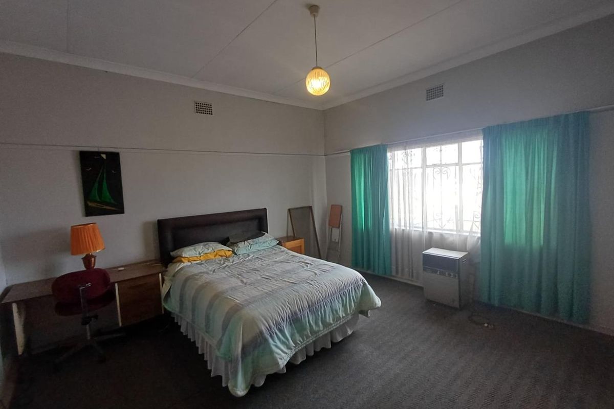 Spacious bedroom featuring large windows with security bars, carpeted flooring, and a built-in air conditioning unit.