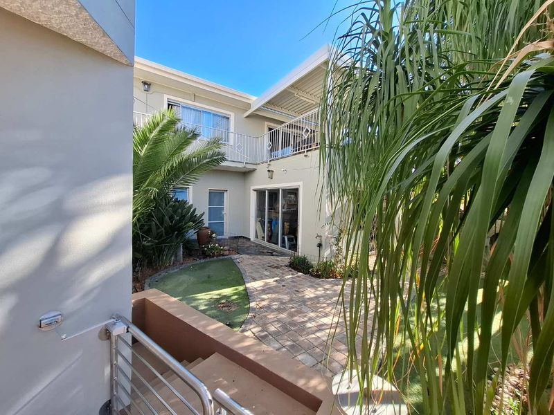 A view of the rear courtyard featuring paved pathways, artificial lawn, and an upper-level balcony with metal railings.