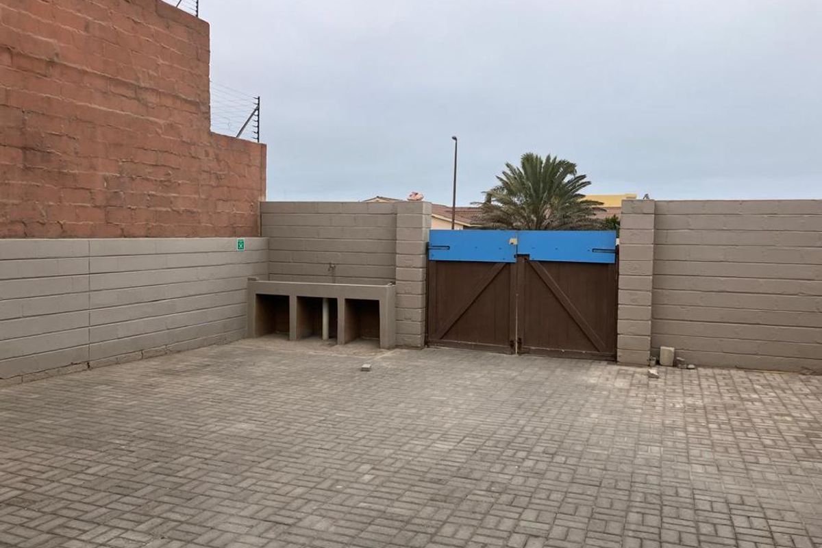 A paved rear courtyard area featuring a built-in concrete wash basin, secure boundary walls with electric fencing, and a double wooden gate.